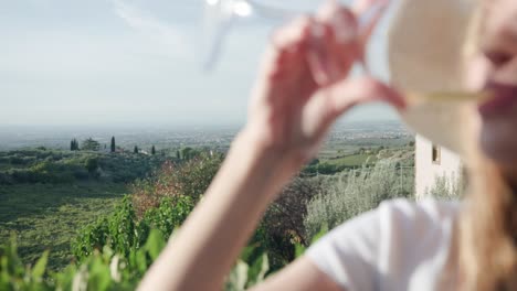 Verschwommenes-Porträt-Einer-Attraktiven-Blonden-Frau-Mit-Hut,-Die-Ein-Glas-Champagner-Trinkt,-Während-Sie-Sich-Im-Freien-Mit-Blick-Auf-Die-Natur-In-Italien-Entspannt