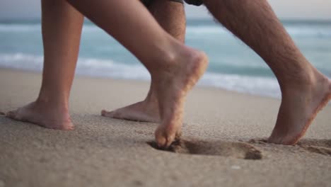 Slow-motion-handheld-shot-of-a-couple-in-love-taking-a-romantic-walk-along-a-sandy-beach-with-calm-waves-in-the-sea