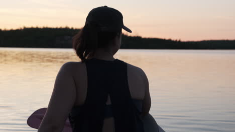 Woman-in-a-canoe-points-across-calm-water-at-golden-hour