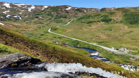 Norewgian-mountain-road-rv-13-seen-from-a-distance-in-idyllic-surroundings-with-river-stream-passing-close-to-camera---Static-handheld-clip-from-Vikafjell-Norway