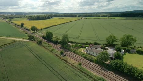 Aerial-view-of-British-rural-scene-with-train-tracks,-agricultural-farmland-and-green-fields