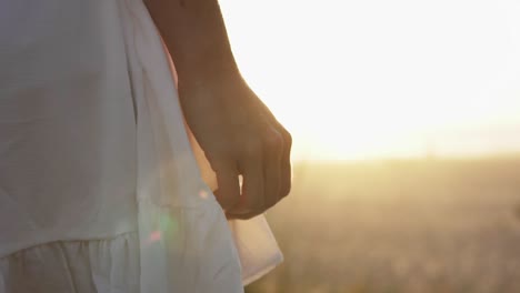 Slow-motion-handheld-close-up-panning-shot-of-a-woman-dressed-in-a-white-dress-standing-on-the-dunes-at-the-beach-during-a-beautiful-sunset-in-the-background
