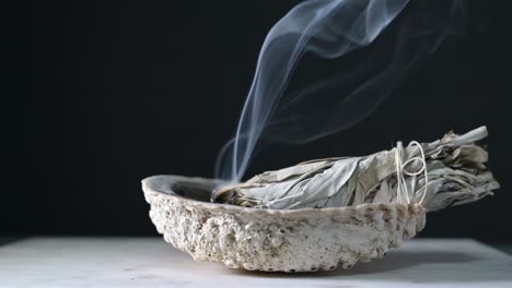 Burning-sage-in-a-shell-on-a-wood-table-with-black-background-showing-sage-smoke