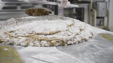 slow-motion-panning-shot-of-a-dough-mass-for-sweets-in-a-candy-factory-in-medina-sidonia-while-a-baker-with-a-metal-tablet-stacks-more-mass