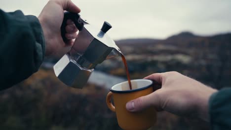 Mannhände-Gießen-Kaffee-In-Reisebecher-Aus-Kaffeekanne-Mit-Naturlandschaft