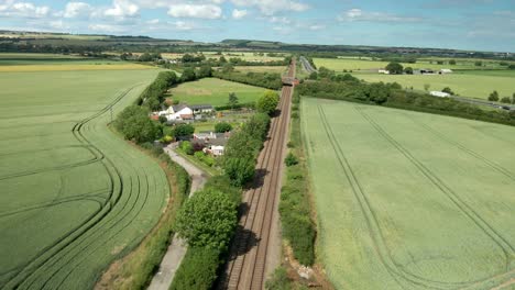Aerial-view-of-train-tracks,-agricultural-farmland-and-green-fields-and-blues-sky