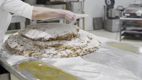 Slow-motion-panning-shot-of-a-pastry-chef-portioning-and-processing-a-mass-or-dough-for-sweets-with-a-metal-tablet