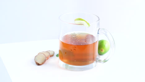 lemon-tea-in-a-transparent-glass-cup-with-whole-and-sliced-lemon-mint-leaves-in-white-background-rotating-side-shot