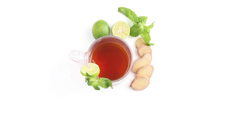 lemon-tea-in-a-transparent-glass-cup-with-whole-and-sliced-lemon-ginger-mint-leaves-in-white-background-rotating-top-shot