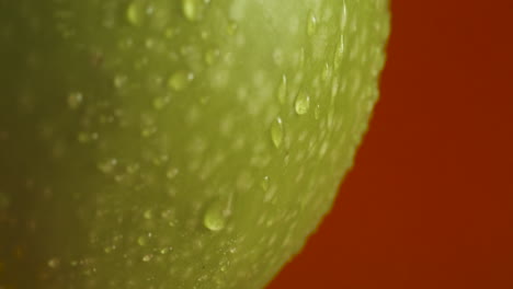 Close-up-shot-of-an-green-apple-with-water-drops-on-it-on-red-background