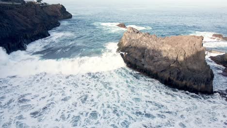 Drone-shot,-top-view-of-big-rock-and-waves-in-Tenerife,-Spain