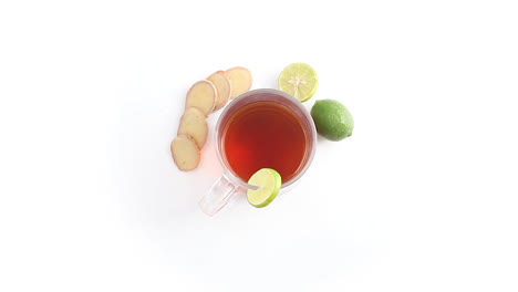lemon-tea-in-a-transparent-glass-cup-with-whole-and-sliced-lemon-ginger-in-white-background-rotating-top-shot