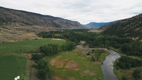 aerial-shot-dolly-forward-over-a-beautiful-nature-landscape-in-Chance-Creek-British-Columbia-with-green-fields-and-a-river-running-through-the-valley-in-a-desert-valley