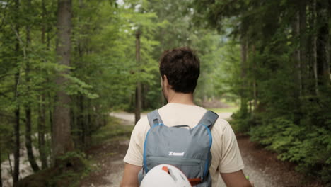 A-young-man-walking-on-a-path-in-the-forest-with-the-grey-backpack-and-white-helmet