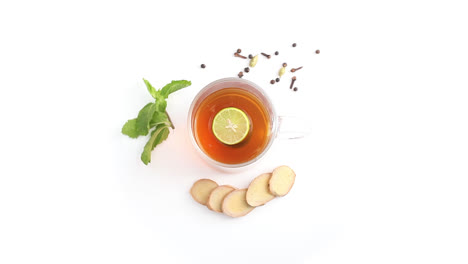 lemon-tea-in-a-transparent-glass-cup-with-whole-and-sliced-lemon-cloves-black-pepper-cardamom-in-white-background-rotating-top-shot