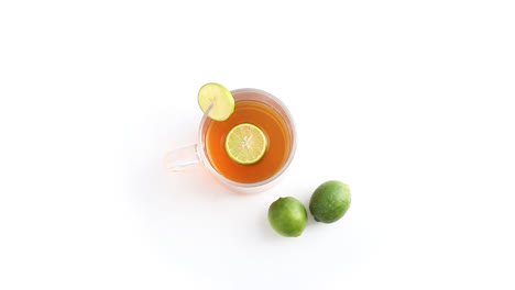 lemon-tea-in-a-transparent-glass-cup-with-whole-and-sliced-lemon-in-white-background-rotating-top-shot
