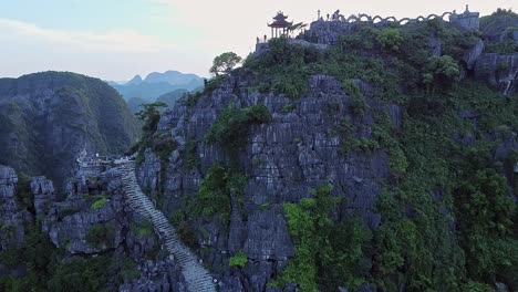 Aerial-View-Of-Stairs-To-Viewpoint-On-Cliff-With-Dolly-Back-Over-Pagoda-With-Tourists-Visiting-At-Ninh-Binh-In-Vietnam