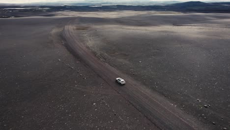 Dron-Siguiendo-Un-Auto-Plateado-Filmado-Desde-La-Izquierda-Conduciendo-Fuera-De-La-Carretera-En-El-Campo-Lunar-De-Islandia-En-4k