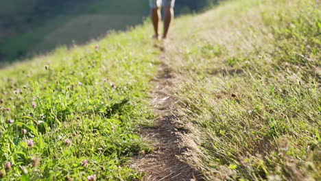 Close-up-in-slow-motion-of-a-small-path-on-a-beautiful-green-meadow,-young-man-walking