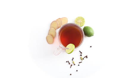 lemon-tea-in-a-transparent-glass-cup-with-whole-and-sliced-lemon-sliced-ginger-cardamom-cloves-black-pepper-in-white-background-rotating-top-shot