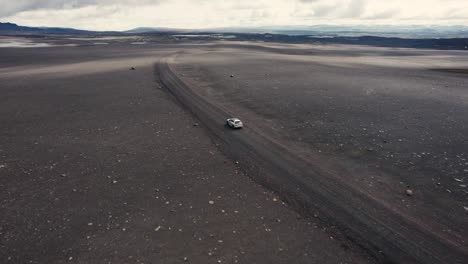 Dron-Siguiendo-Un-Coche-Plateado-Con-La-Cámara-Inclinándose-Lentamente-Conduciendo-Fuera-De-La-Carretera-En-El-Campo-Lunar-De-Islandia-4k