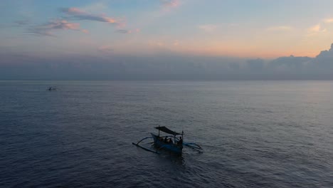Antenne-Des-Wunderschönen-Jukung-Bootes,-Das-Während-Des-Sonnenaufgangs-Der-Goldenen-Stunde-In-Lovina-Bali,-Indonesien,-Auf-Dem-Flachen,-Endlosen-Blauen-Ozean-Schwimmt