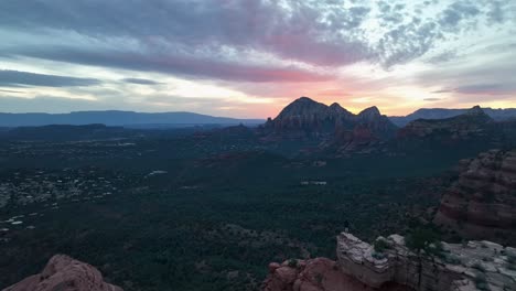Tourist-Standing-On-The-Edge-Of-The-Cliff,-Enjoying-Scenic-Landscape-Of-Sedona-In-Arizona-At-Sunset---aerial-drone-shot