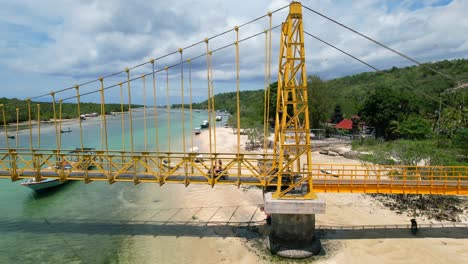 arial-parallel-of-two-tourists-driving-scooters-across-yellow-suspension-bridge-in-Nusa-Ceningan-and-Nusa-Lembongan-island-in-Bali-Indonesia