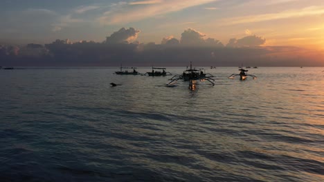 Antenne-Von-Schönen-Fischerbooten-Am-Horizont,-Wenn-Die-Sonne-Aufgeht-Und-Delfine-Aus-Dem-Blauen-Ozean-In-Lovina-Bali-Indonesien-Springen
