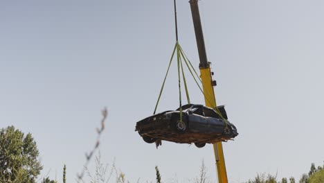 Low-angle-shot-of-a-crane-lifting-an-old-wrecking-car-from-a-junkyard-in-daylight