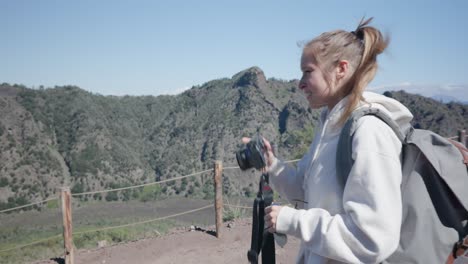 Side-View-Of-Cute-Young-Tourist-Girl-With-Backpack-Holding-A-Camera-Taking-Pictures-At-The-Countryside-Nature-On-A-Nice-Sunny-Day