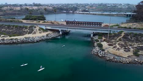Paddle-boarders-in-Carlsbad-lagoon,-drone-view-on-looking-I-5-North,-I-5-South