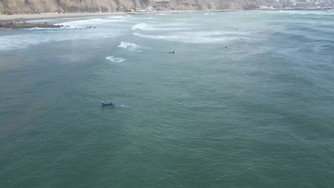 Aerial-shot-of-the-turquoise-sea-in-miraflores-in-peru-lima-with-surfers-with-surfboards-in-the-water-swimming-during-calm-waves-on-a-sunny-day