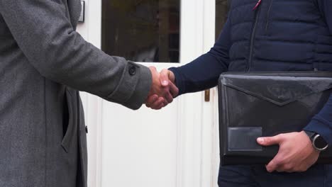 Two-businessmen-shaking-hands-with-document-binder-in-front-of-the-door