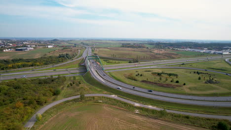 Vista-Aérea-Del-Tráfico-En-La-Carretera-De-Autopista-De-Nueva-Construcción-Durante-El-Día-Soleado-Y-El-Puente-De-Intersección