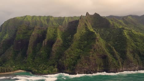 Beautiful-nature-view,-drone-flying-over-green-jungle-mountain-peaks-revealing-tropical-beach-on-NaPali-park-4K