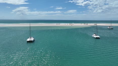 Flying-over-the-water-between-catamaran-boats-towards-vehicles-parked-on-sandbar