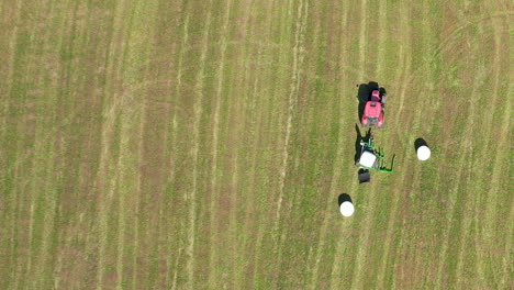 Top-View-Of-Green-Agricultural-Field-With-Tractor-And-White-Bales-Of-Hay---drone-shot