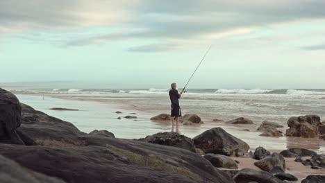 Recreational-fisherman-stands-on-the-beach-sand-while-fishing-in-the-surf