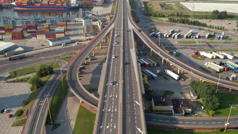 Aerial-tilt-up-shot-of-cars-driving-on-highway-near-Harbor-of-Gdynia-with-docking-container-ships,Poland