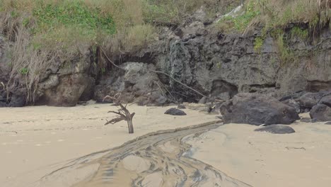 small-waterfall-flows-off-sand-dune-over-black-beach-rock-and-flows-into-the-ocean