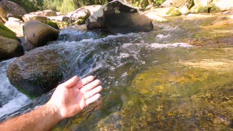 A-man's-hand-moving-in-the-stream-of-clean-water-from-a-waterfall