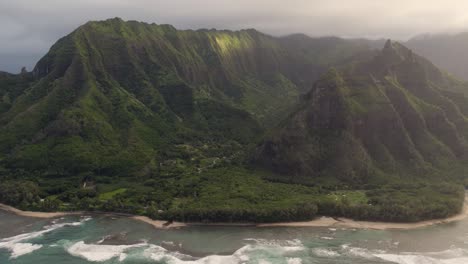 Epic-aerial-above-Hawaii-coast-landscape-of-Haena-park,-panoramic-views-on-Na-Pali-coast-park-with-green-jungle-mountain-peaks-covered-by-rain-clouds