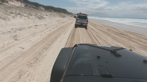 Ein-Schwarzer-Jeep,-Der-Auf-Weichem-Strandsand-Fährt-Und-Anderen-4x4s-Folgt,-Wenn-Die-Flut-Steigt