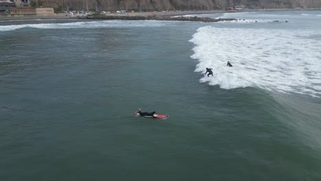 Luftschwenk-Aus-Dem-Niedrigen-Winkel-Auf-Das-Meer-Mit-Wellen-In-Miraflores-Lima-In-Peru-Mit-Surfer-Auf-Einem-Surfbrett-Und-Anderen-Menschen,-Die-Aufs-Meer-Hinausschwimmen