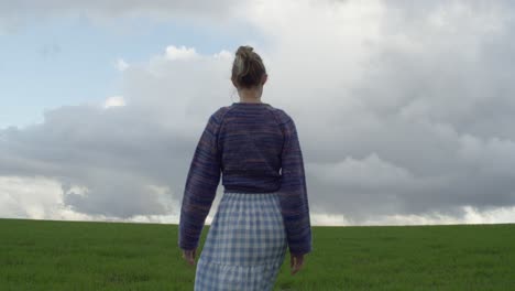 A-Young-Woman-Walking-Through-A-Green-Field-on-An-Overcast-and-Moody-Day,-Slow-Motion