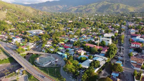 Daily-activities-and-sights-within-capital-city-Dili,-Timor-Leste-in-Souheast-Asia,-people-playing-football,-traffic-moving-along-roads-and-view-of-protective-rugged-hilly-landscape,-aerial-drone