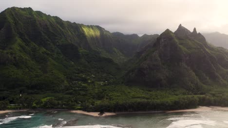 Epic-aerial-above-Hawaii-coast-landscape-of-Haena-park,-panoramic-views-on-NaPali-park-with-green-tropical-jungle-mountain-peaks-covered-by-rain-clouds
