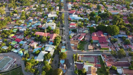 Aerial-drone-rising-over-inner-city-view-of-capital-Dili,-Timor-Leste-in-Southeast-Asia,-residential-houses-with-colorful-tinned-roofs,-businesses-and-tree-greenery-with-traffic-traveling-along-road