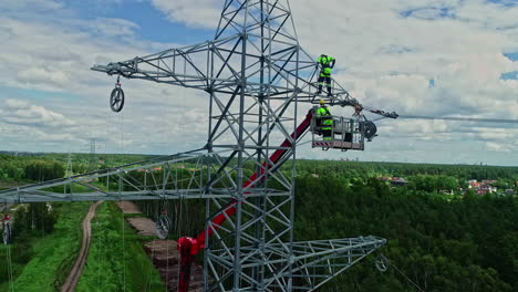 Parallex-drone-shot-of-technicians-on-lifting-crane-working-on-high-voltage-electricity-tower-in-their-uniform